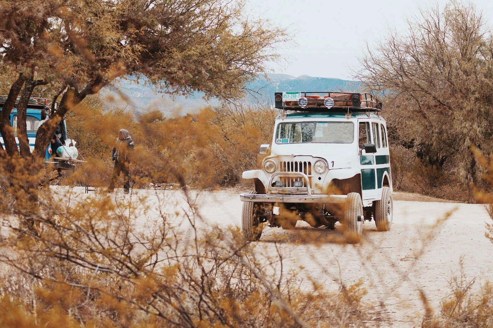 A classic jeep parked on a sandy road surrounded by trees in Real de Catorce, Mexico.