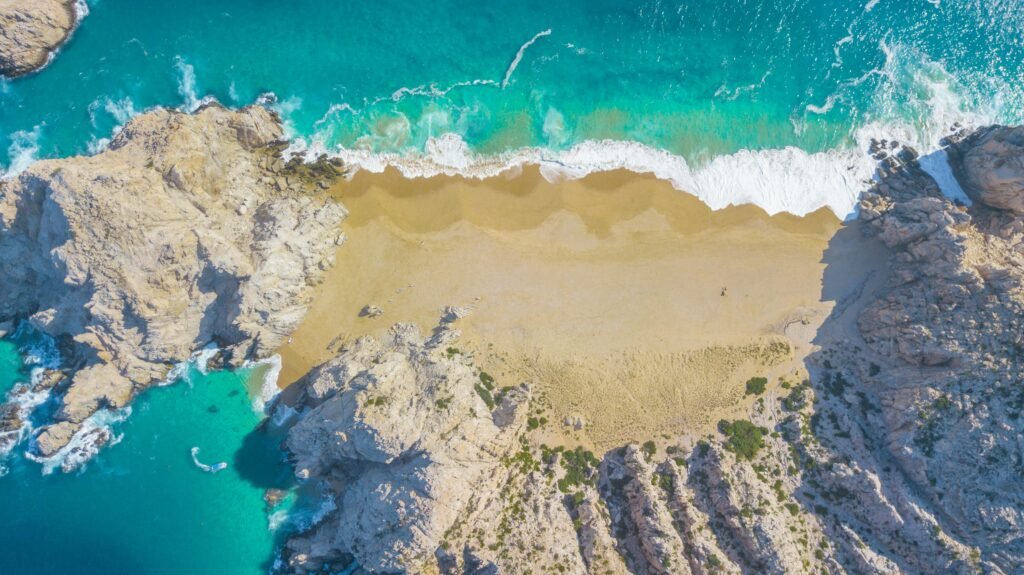 A stunning aerial view of Divorce Beach in Cabo San Lucas, showcasing turquoise waters and golden sands.