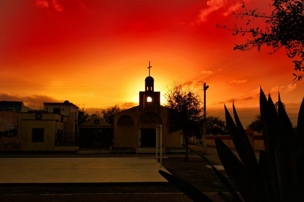 Silhouetted church with a cross against a dramatic sunset sky, showcasing vibrant colors and cultural architecture.